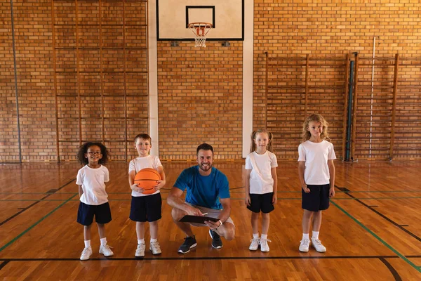 在篮球场上看镜头的快乐篮球教练和小学生的正面观点 — 图库照片