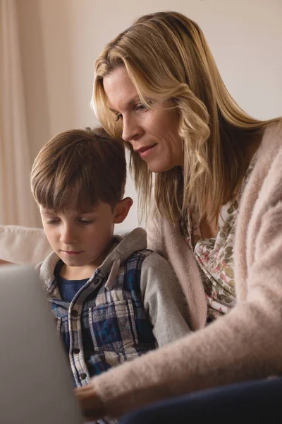 集中的母亲帮助儿子在家里的客厅里使用笔记本电脑的正面看法 — 图库照片