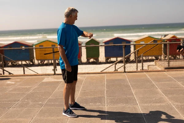 在海滩长廊上的智能手机上积极的高级男子检查时间的侧视图 — 图库照片