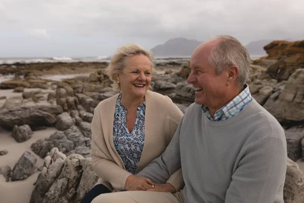 活跃的高级夫妇在海滩上坐在背景中的山上互动的侧视图 — 图库照片