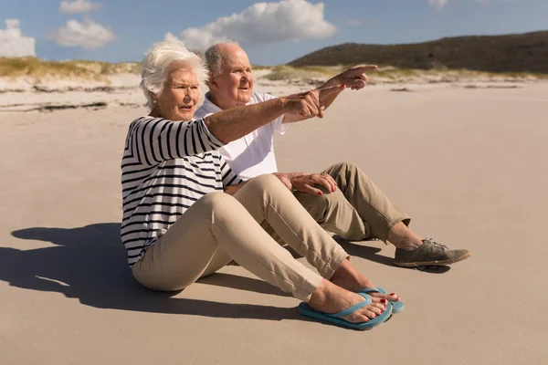 Boční Pohled Starší Pár Ukazuje Vzdálenosti Při Posezení Pláži Slunci — Stock fotografie