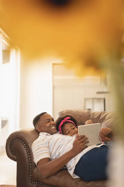 快乐的非裔美国人父女俩在沙发上放松 在家中使用数字平板电脑的侧视图 — 图库照片