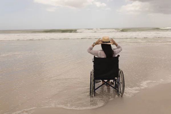 無効になっている若い女性帽子を押しながらビーチで車椅子に座っての背面図 — ストック写真