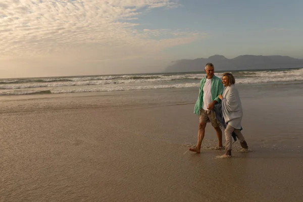 手をつないでビーチを歩いてアクティブ シニア カップルの側面図 — ストック写真