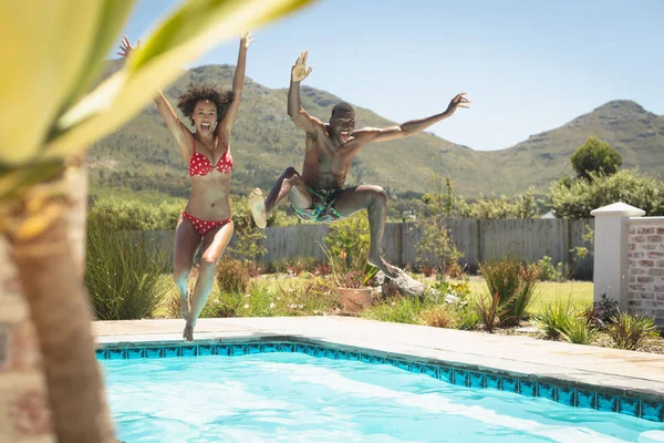 晴れた日に 彼らの裏庭のプールでジャンプ幸せな若いアフリカ系アメリカ人カップルの肖像画 — ストック写真