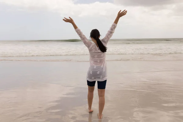 在阴天 一个白种人妇女站在沙滩上看大海的后视镜 — 图库照片