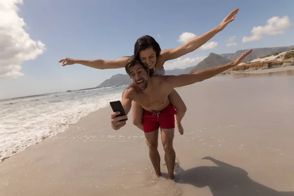 Framifrån Lyckliga Unga Paret Piggyback Med Armarna Utsträckta Tar Selfie — Stockfoto