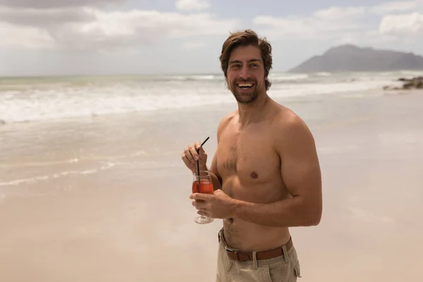 カクテルを見て太陽の下 ビーチのカメラで上半身裸の幸せな若い男の正面図 — ストック写真