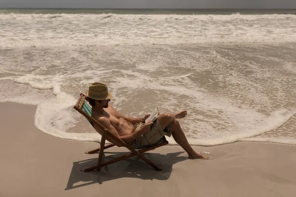 サンラウン ジャーでリラックスしたり 太陽の下 ビーチでノート パソコンを使用する帽子と上半身裸の若い男のハイアングル — ストック写真