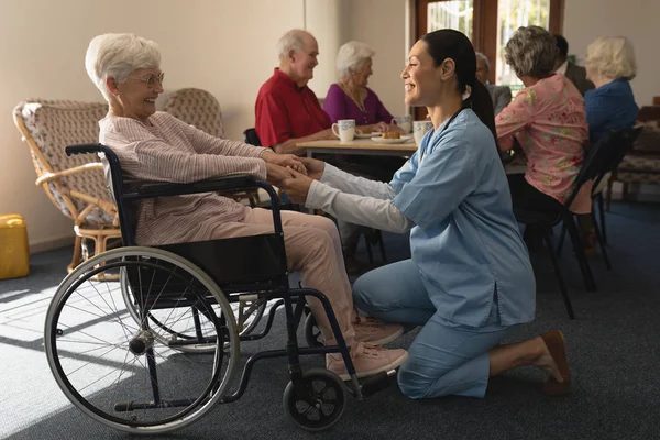 愉快的女医生牵手 在家中与残疾的老年妇女交谈的侧视图 — 图库照片