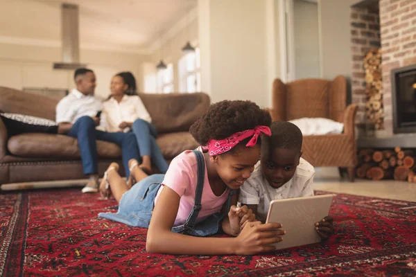 当父母坐在家里的沙发上时 快乐的非洲裔美国孩子躺在地板上 使用数字平板电脑的侧视图 — 图库照片