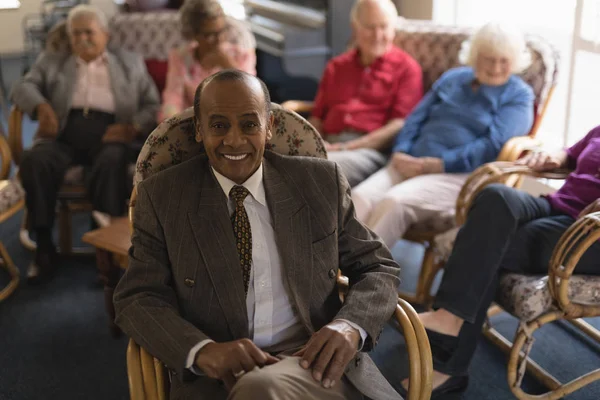 Front view of happy senior man looking at camera with his friends behind his in nursing home