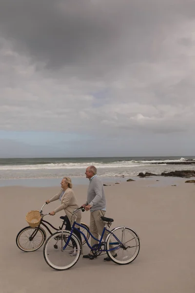 活跃的资深夫妇的侧视图与自行车走在海滩与海洋的背景 — 图库照片