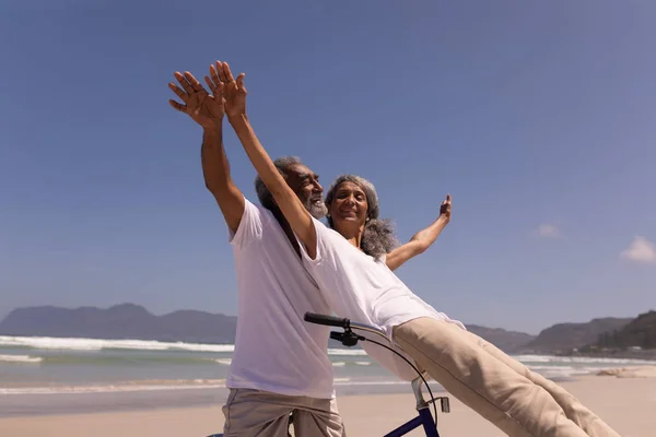 快乐的老人骑自行车的低角度的角度来看 在阳光下 高级女子坐在沙滩上 背景是山 — 图库照片