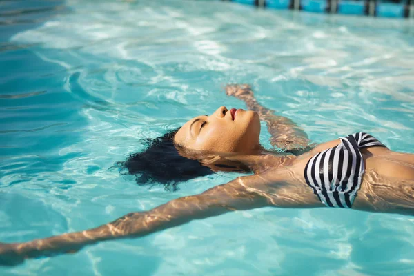 年轻混血女子在家里后院游泳池里漂浮的侧视图 — 图库照片