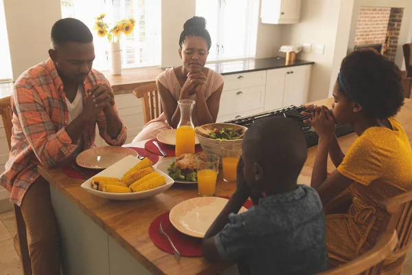 アフリカ系アメリカ人の家族の手で前面展望を握りしめ 快適な自宅のダイニング テーブルで一緒に祈っている閉じた目 — ストック写真