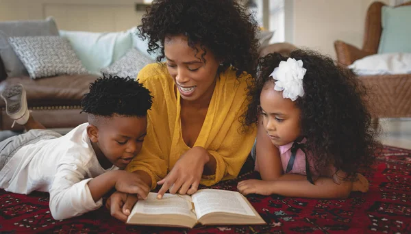 非洲裔美国母亲和她可爱的孩子躺在地板上 在舒适的家里看书的正面 — 图库照片