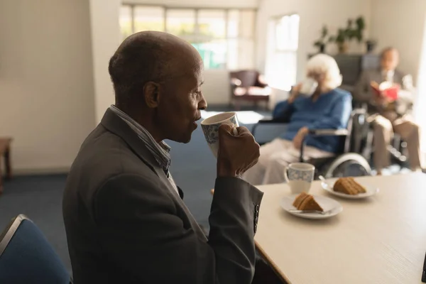 在家里的餐桌上 老人和他身后的朋友一起在前景中喝咖啡的侧视图 — 图库照片