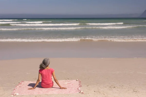 在阳光下坐在沙滩上的老年妇女的后视 — 图库照片
