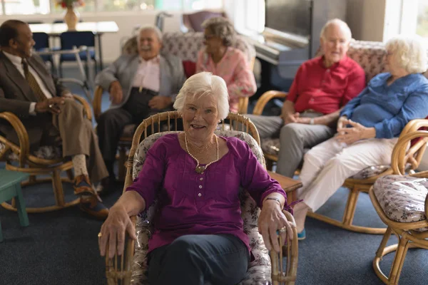 Front view of happy senior woman looking at camera with her friends behind her in nursing home