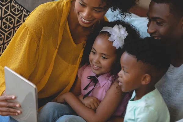 在舒适的家中 在沙发上使用数字平板电脑 让可爱的孩子和他们可爱的孩子在一起的快乐的非裔美国人父母的正面看法 — 图库照片