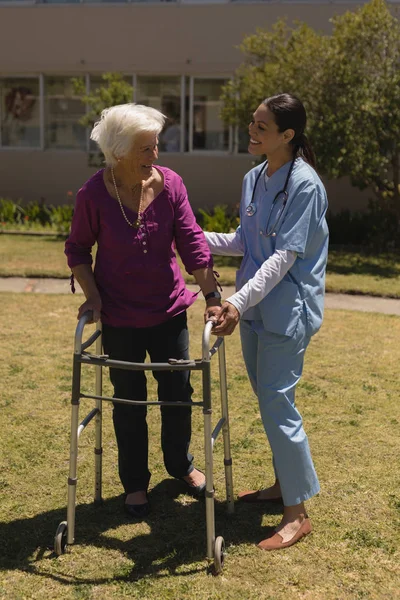 阳光明媚的日子里 年轻女医生在花园里帮助残疾老年妇女的前景 — 图库照片