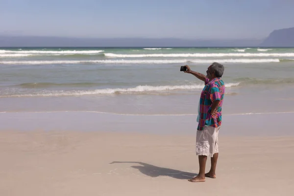太陽の下 ビーチでの携帯電話で Selfie を取って幸せな年配の男性の側面図 — ストック写真