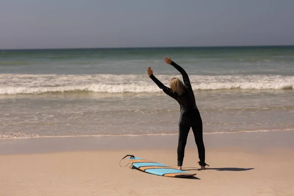 ビーチでサーフボードを動かせることとシニアの女性サーファーの背面図 — ストック写真
