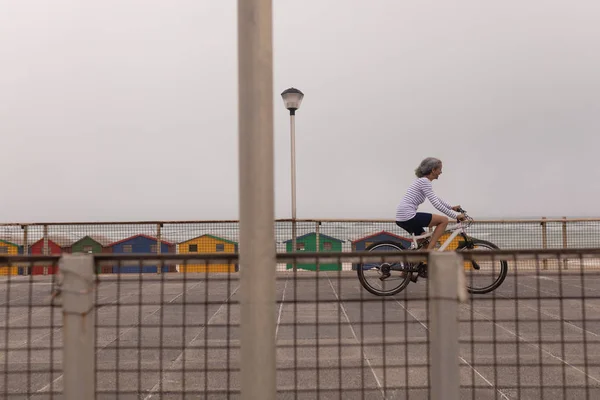 在海滩上的长廊上骑自行车的老年妇女的侧视图 — 图库照片