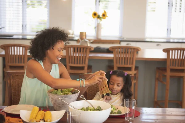 非洲裔美国母亲在舒适的家中的餐桌上为女儿提供沙拉的正面看法 — 图库照片