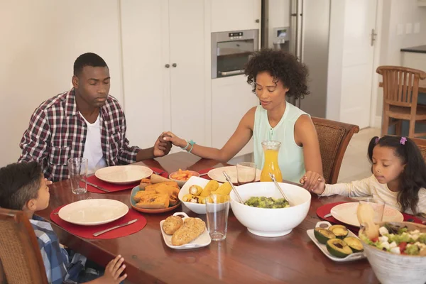 目と手を保持しているアフリカ系アメリカ人の家族のフロント ビューが快適な家にダイニング テーブルで一緒に祈りながら閉じ — ストック写真