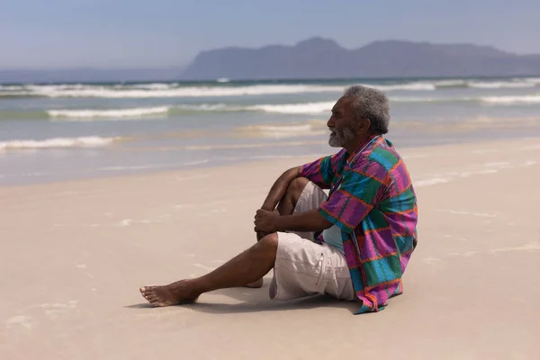 Widok Boczny Rozważny Człowiek Starszy Siedząc Plaży Promieniach Słońca — Zdjęcie stockowe