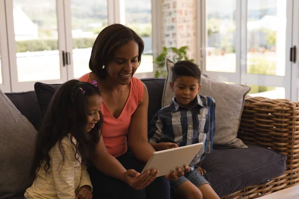 在家中的客厅里 坐在柳条沙发上 用数字平板电脑欣赏快乐的多代家庭的正面景观 — 图库照片