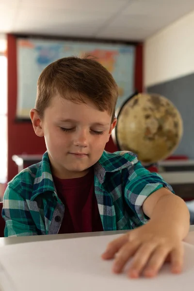 小学校の教室の机に点字本を読んで白人視覚障害の少年の正面図 — ストック写真