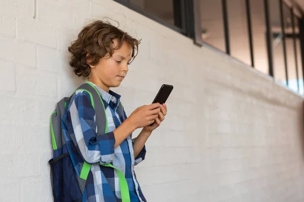 学校の廊下の壁にもたれながら彼の携帯電話を使用して白人少年の側面図 — ストック写真