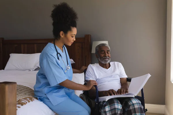 一个盲人非洲裔美国高级男子在家中与年轻的非洲裔美国女医生一起读盲文的正面观点 — 图库照片
