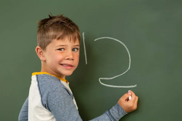 小学校の教室で緑の黒板に数学をやってかわいい少年の正面図 — ストック写真
