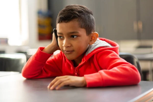 Framifrån Söt Blandad Ras Skolpojke Pratar Mobiltelefon Skrivbord Ett Klassrum — Stockfoto