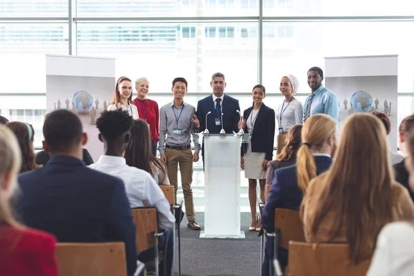 事務所ビルにビジネス セミナーで話している間に表彰台に立ってビジネス人々 の多様なグループの正面図 — ストック写真