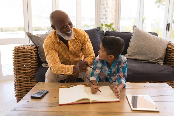 一个骄傲的非洲裔美国祖父在家里的客厅里帮孙子做作业的正面看法 — 图库照片