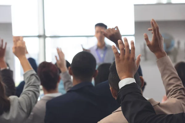 Rear view of diverse business people raising hands in a business seminar in office building