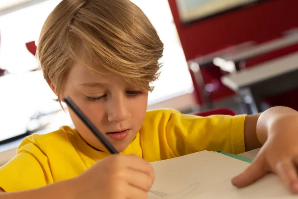 小学校の教室の机で本のスケッチを描く白人少年の正面図 — ストック写真