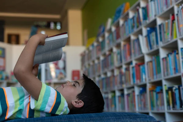 Vista Lateral Colegial Caucásico Acostado Sofá Leyendo Libro Biblioteca Escuela — Foto de Stock