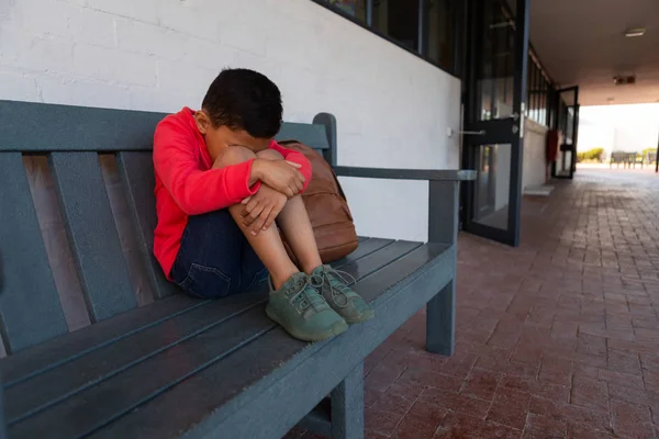 Vista Frontal Colegial Mestiço Triste Sentado Sozinho Banco Corredor Escola — Fotografia de Stock