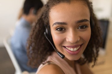 Portrait of beautiful mixed-race female executive in headset smiling in office. She seems happy clipart