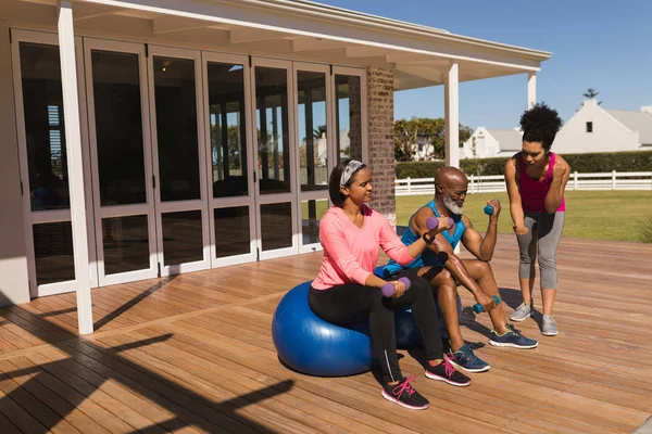 家の裏庭にダンベルと運動ボール運動を実行することで若いフィットは アフリカ系アメリカ人女性パーソナル トレーナー トレーニング上級アフリカ系アメリカ人カップルの正面図 — ストック写真