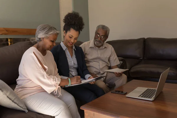 在家里客厅的沙发上 一名非洲裔美国高级妇女与房地产经纪人和高级男子签订了财产合同的侧视图 — 图库照片