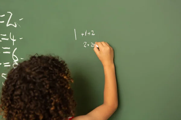 学校の教室で緑色の基板上の数学計算の解決混血少年の後姿 — ストック写真