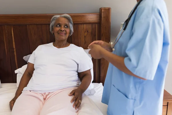 自宅の寝室で若いアフリカ系アメリカ人女性医師と対話する年配のアフリカ系アメリカ人女性の正面図 — ストック写真