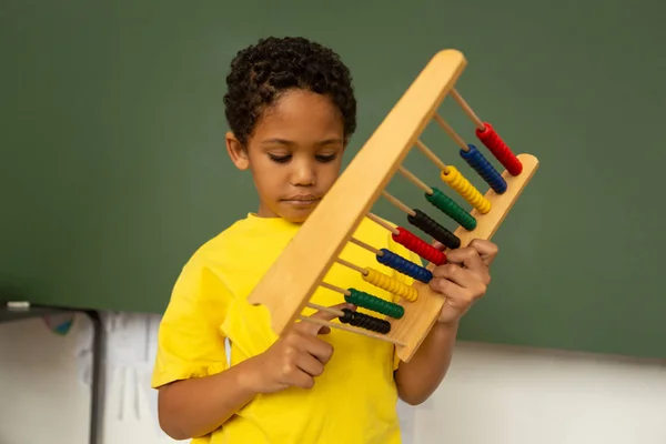 小学校の教室でそろばんを使った数学学習思慮深い混血少年の正面図 — ストック写真